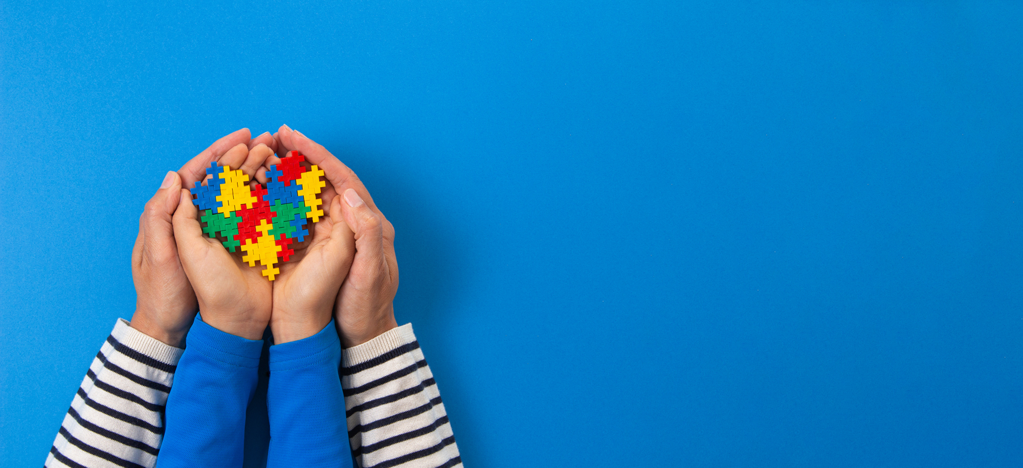 World autism awareness day concept. adult and child hands holding puzzle heart on light blue background