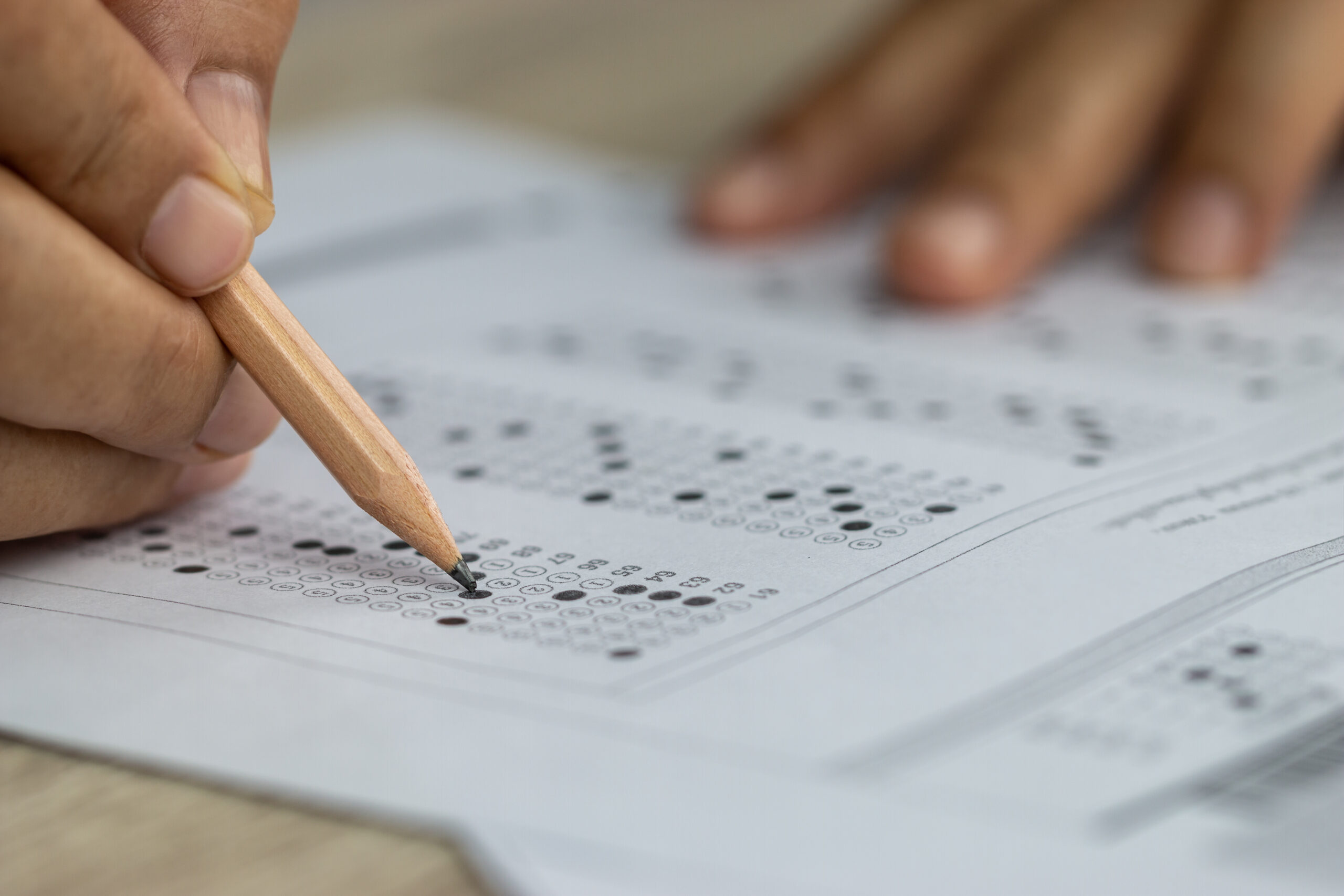 School students hands taking exams, writing examination holding pencil on optical form of standardized test with answers sheet doing final exam in classroom. education assessment concept. soft focus