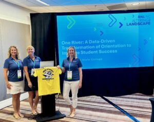 The photo shows Elizabeth Gaskin, Emily Mass, and Rebecca Shearer at a podium at the Ruffalo Noel Levitz Conference. 