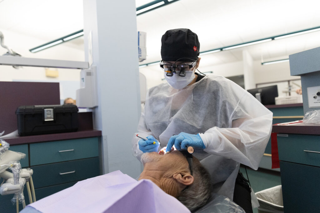 A dental hygiene student wearing protective gear, gloves, and magnifying loupes performs a cleaning on a patient in a clinical lab setting at Indian River State College.