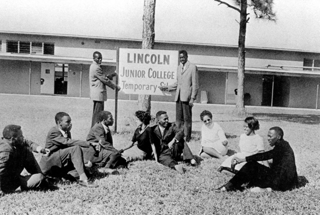 A black and white photo of students outside a building beneath a sign reading "Lincoln Junior College" in 1960.