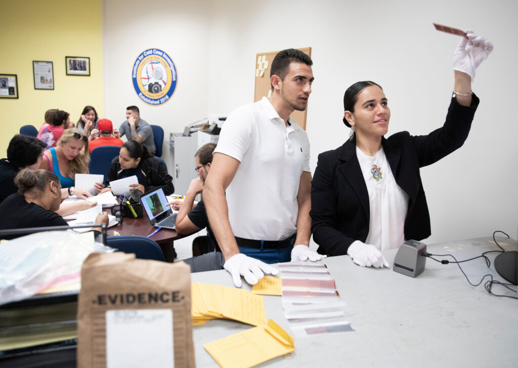 A photo of two students in the foreground. One student holds up an evidence slide, as they both gaze at the slide.