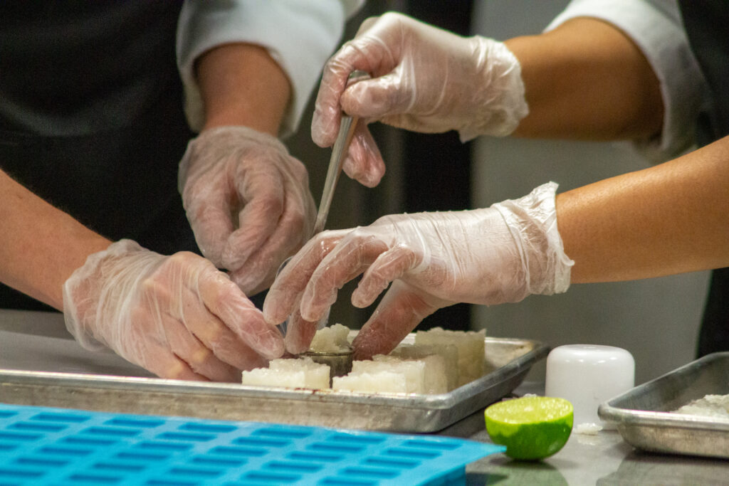 A photo of two gloved hands placing food items on a tray.