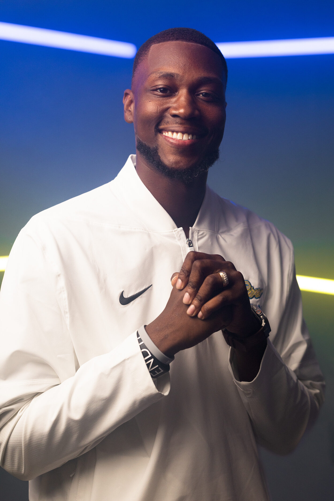 Smiling man in a white Nike jacket stands under dramatic blue and yellow lighting, representing Indian River State College Men’s Basketball Head Coach Travis “T.J.” Jackson.