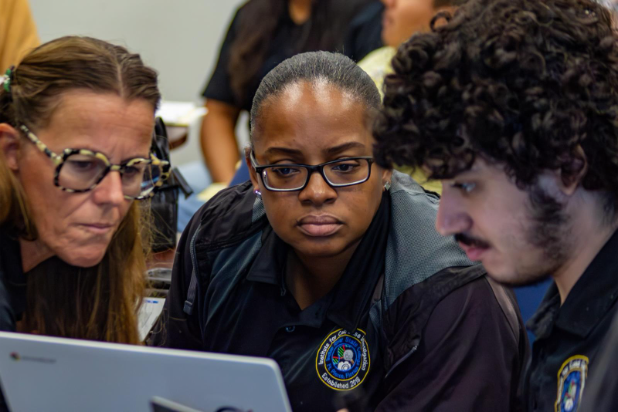 A photo of three students intently looking at a computer monitor.
