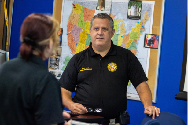 A photo of an Indian River County Sheriff's investigator standing behind a map while speaking with Dr. Kimberlie Massnick in a classroom.