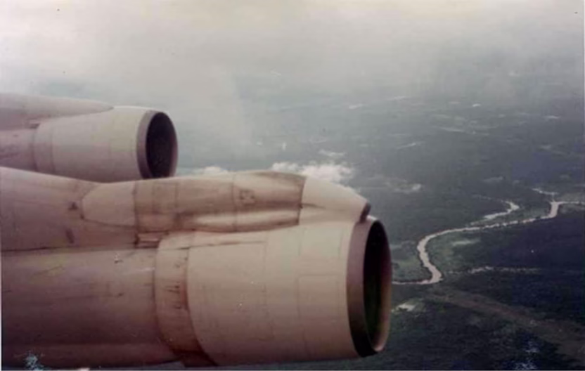 View from aircraft window showing jet engines and wing overlooking Vietnamese landscape below during departure flight in 1967