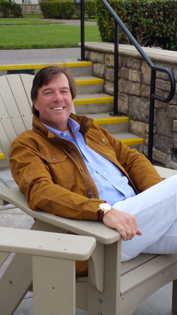 Person in mustard-colored jacket and light blue shirt sitting in white Adirondack chair near stone steps with yellow safety edging and black handrails